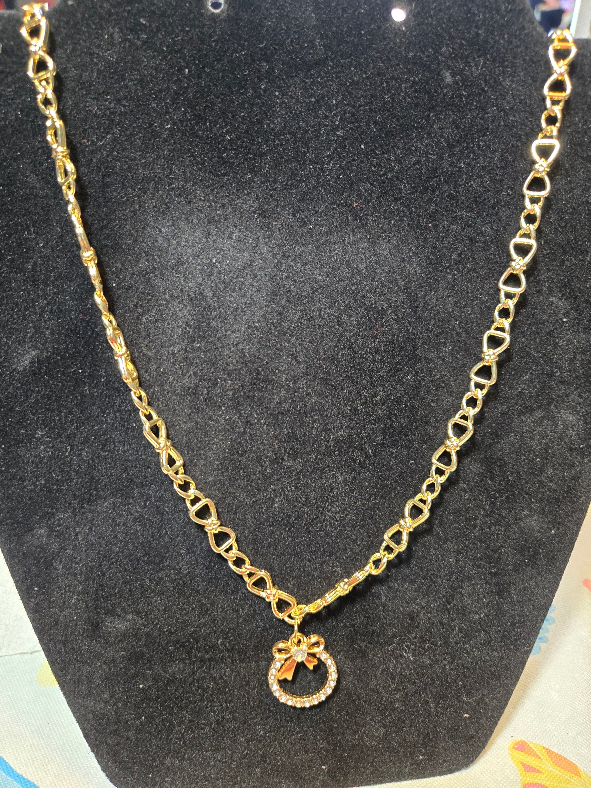 Gold toned, Bow necklace with small white gemstones in a circular pattern, topped with a gold bow