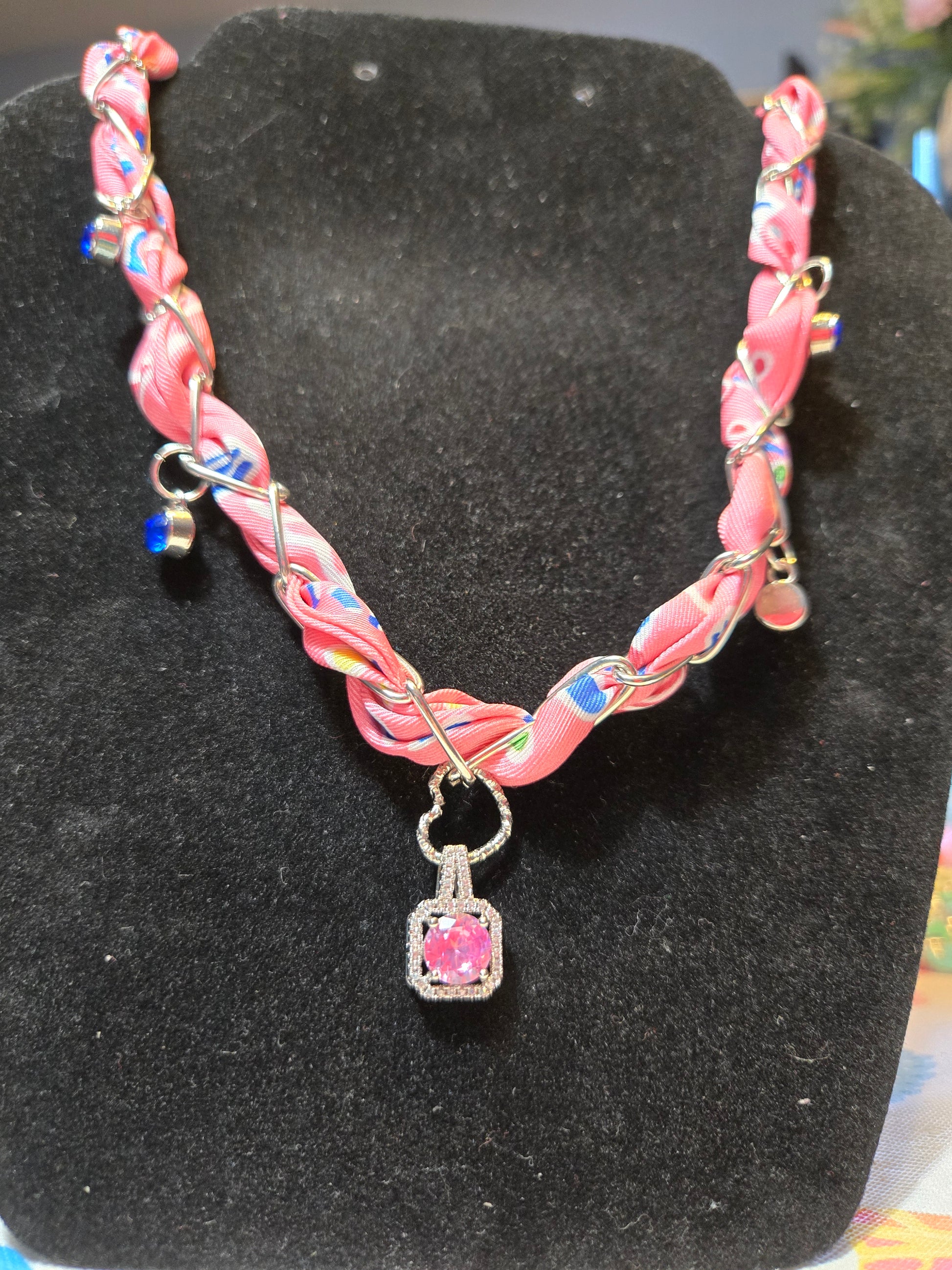 Pink scarf in a paperclip design necklace with blue stone charms for accents and pink gemstone center pendant suspended by a silver heart.